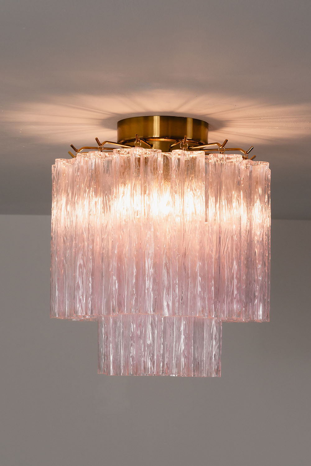 Seraphine Starburst Glass Tube Ceiling Light | Pink Glass and Brass | Studio display showing the chandelier glowing warmly against a dark grey wall | vexa lamps