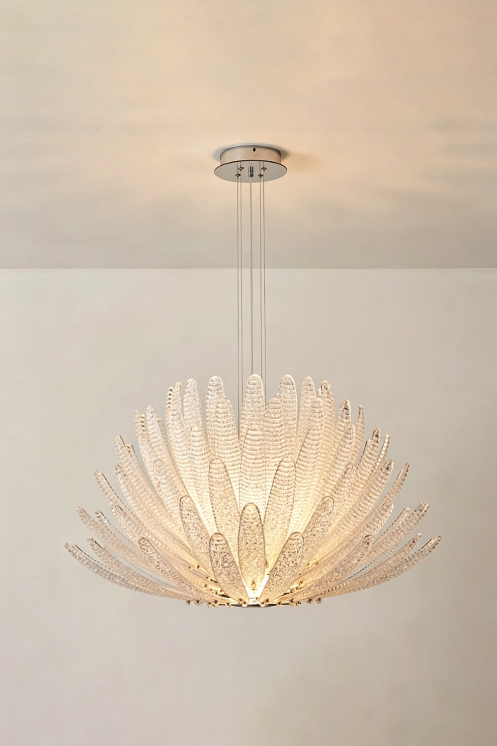 Helios Agave Glass Starburst Chandelier | Glass, Metal | Clear glass variant lit against a light neutral wall, creating a soft white ambiance | Isolated shot | vexa lamps