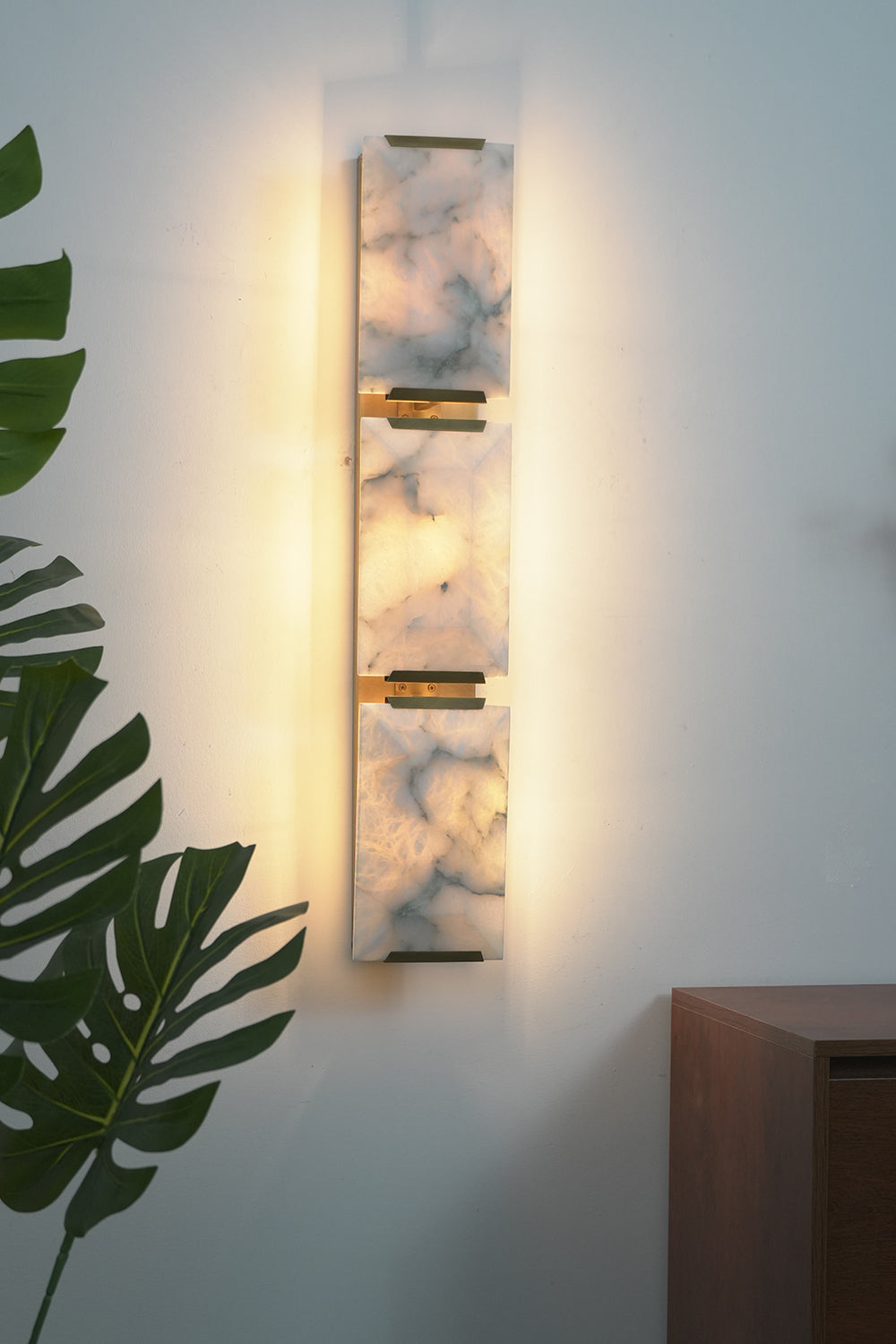 Lit 3-panel alabaster wall lamp | Brass, Alabaster | Perspective view against a white wall with indoor plants | vexa lamps
