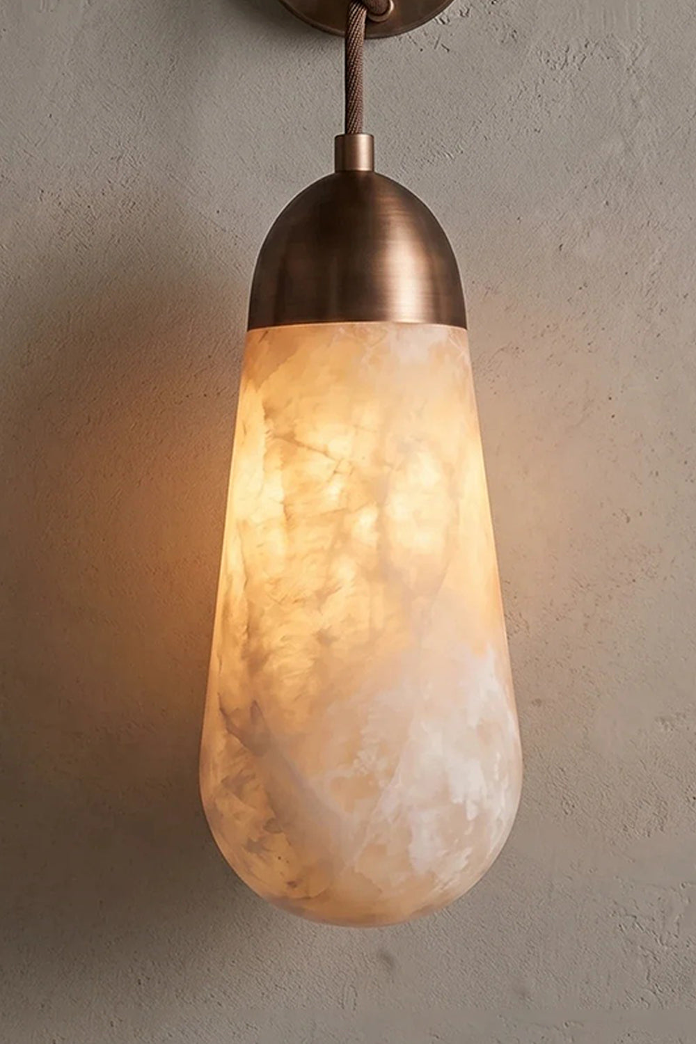 Alabaster Teardrop Wall Sconce with warm light and a textured metal backplate, showcasing natural alabaster veining.