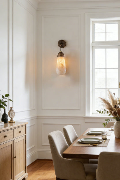 Alabaster Teardrop Wall Sconce illuminating a dining area with elegant decor and natural light.