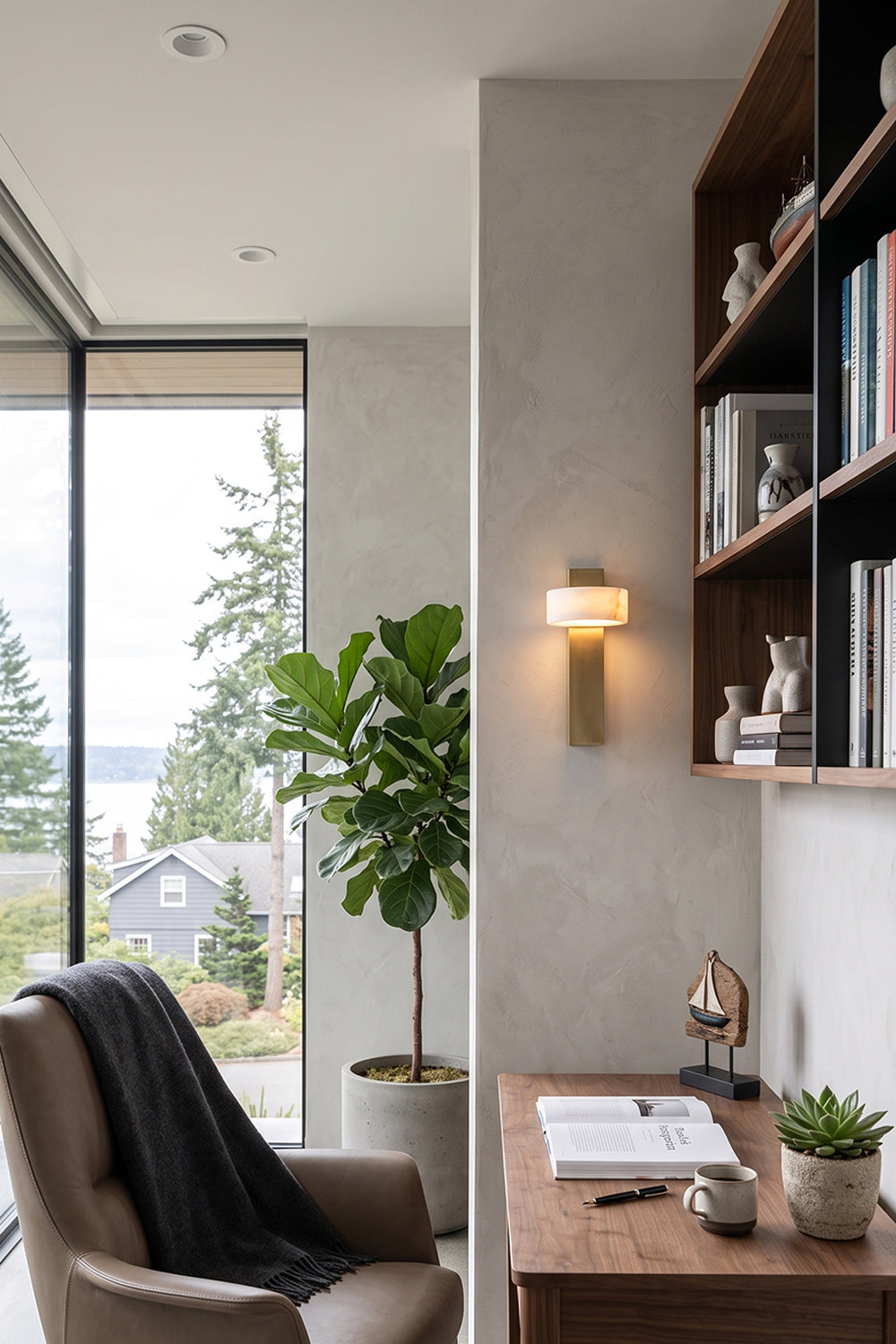 Alaric Alabaster Bar Wall Sconce | Natural Alabaster and Brass | Fixed on a home office wall next to a large dark wood bookshelf and a cozy leather armchair | vexa lamps