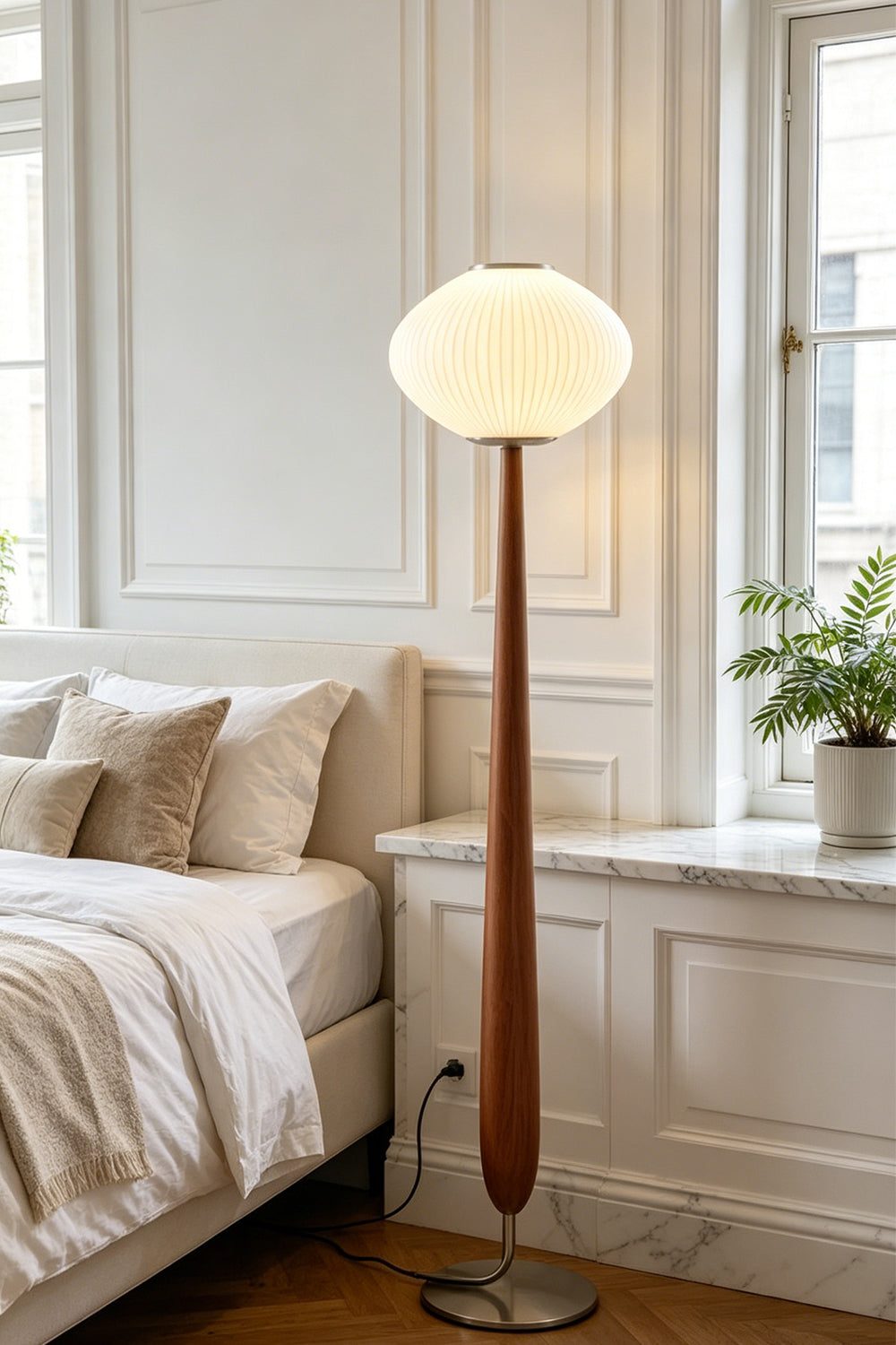 Arden Walnut Floor Lamp | Wood, Metal, Fabric | Providing soft bedtime ambient illumination in a cozy bedroom corner next to a cream platform bed and white paneled walls | vexa lamps