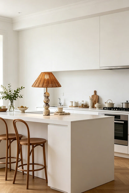 Aria Rattan & Stacked Marble Table Lamp on a kitchen island with white cabinetry and wooden chairs.
