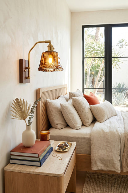 Arlo Amber Ripple Wall Lamp | Glass, Metal, Wood | Mounted above a light wood nightstand, casting cozy illumination over a classical bed setup with plush pillows | vexa lamps
