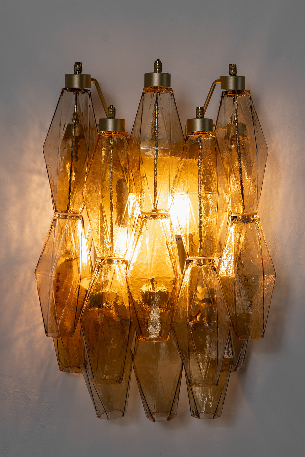 Lit amber polyhedral glass wall lamp | Metal, Glass | High-contrast shot against a dark grey background | vexa lamps