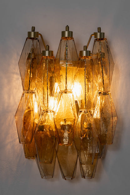 Lit amber polyhedral glass wall lamp | Metal, Glass | High-contrast shot against a dark grey background | vexa lamps