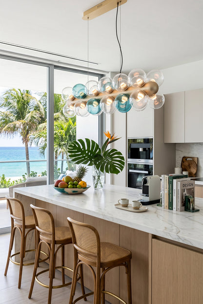 Astraea Linear Prismatic Globe Chandelier hanging above a modern kitchen island with ocean view and tropical decor.