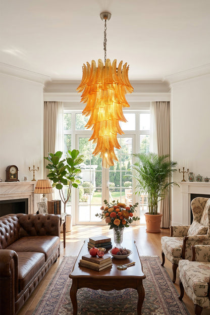 Aurelia Helix Amber Glass Cascade Chandelier illuminating a stylish living room with brown leather couch and green plants.