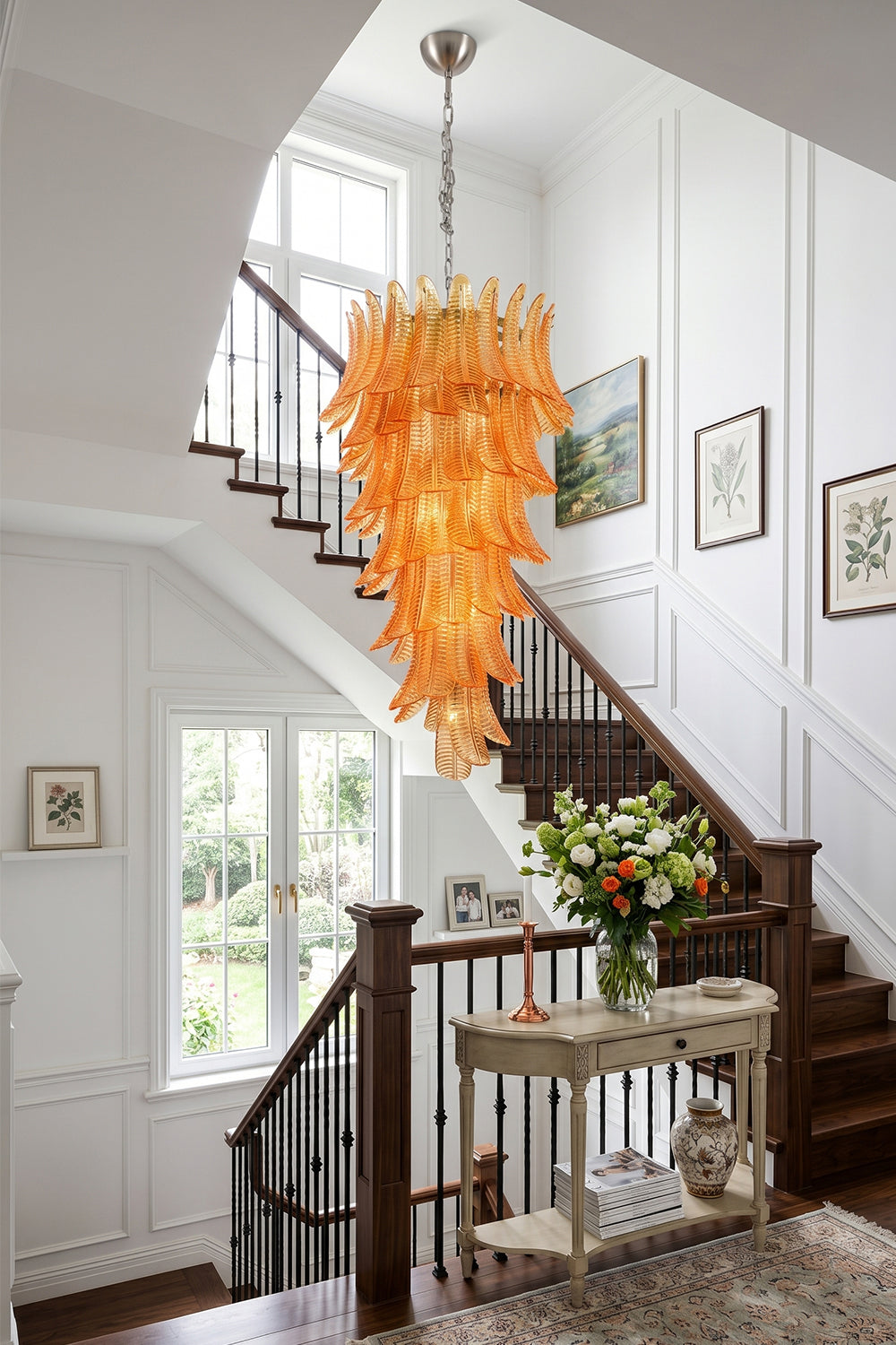 Aurelia Helix Amber Glass Cascade Chandelier illuminating a stylish foyer with elegant staircase and floral decor.