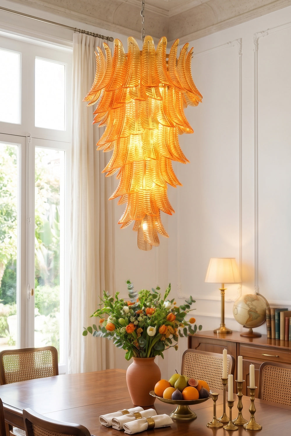 Aurelia Helix Amber Glass Cascade Chandelier illuminating a bright dining room with floral arrangements and fruits.