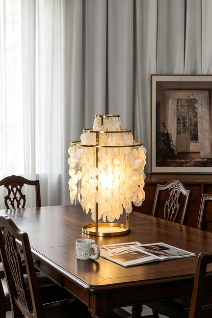 Aurelia Tiered Capiz Table Lamp | Capiz Shell, Metal | Providing a warm golden glow on a long dark wood dining table in a classic traditional dining room | vexa lamps