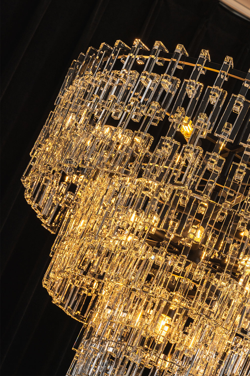 Aven Tiered Glass Prism Chandelier | Glass, Metal | Dramatic close-up under low lighting showing the crystal tiers radiating an intense, warm golden light halo | Detail shot | vexa lamps