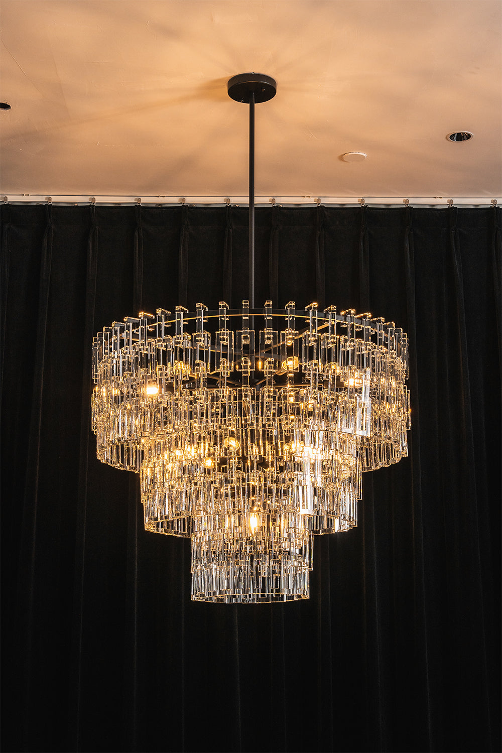 Aven Tiered Glass Prism Chandelier | Glass, Metal | Centered view of the fully illuminated black tier variant casting warm ambient light against a solid dark backdrop | vexa lamps