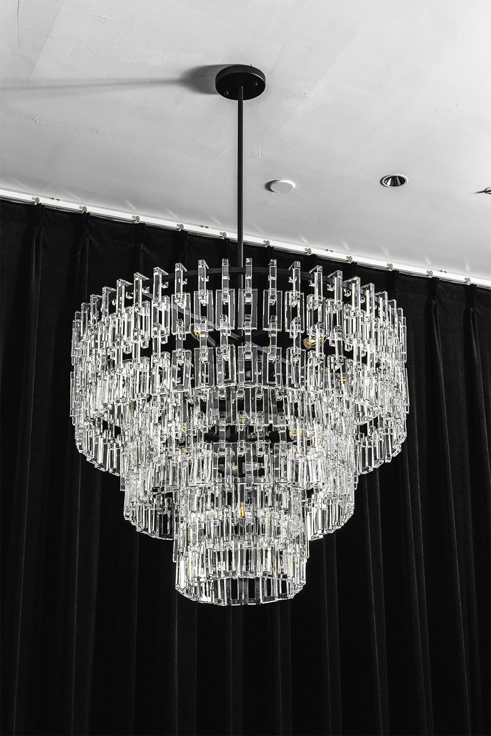 Aven Tiered Glass Prism Chandelier | Glass, Metal | Frontal centered shot of the unlit black metal and clear glass link chandelier variant on a dark studio background | vexa lamps