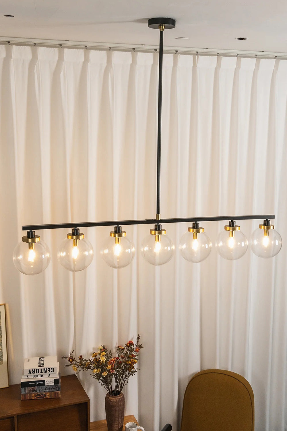 Brooks Linear Glass Globe Chandelier | Glass, Metal | Staged presentation of the fully illuminated multi-light linear island fixture glowing warmly against floor-to-ceiling white drapes | vexa lamps