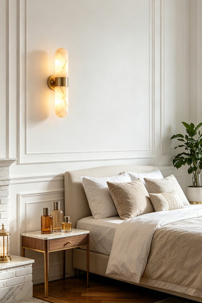 Calla Alabaster Capsule Wall Sconce | Alabaster, Brass | Serving as a cozy bedside reading lamp on a white wall beside a classic platform bed and a wooden nightstand | vexa lamps