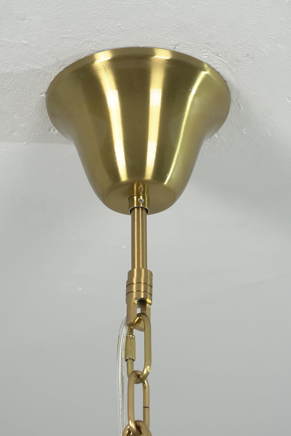 Brass ceiling canopy and chain connection detail | Metal | Close-up of the gold-finish mounting hardware | vexa lamps