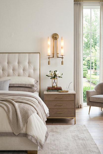 Chantal Twin Alabaster Wall Sconce | Alabaster, Brass | Mounted as a twin-light elegant bedside lamp casting a warm golden ambient glow next to a tufted cream headboard | vexa lamps
