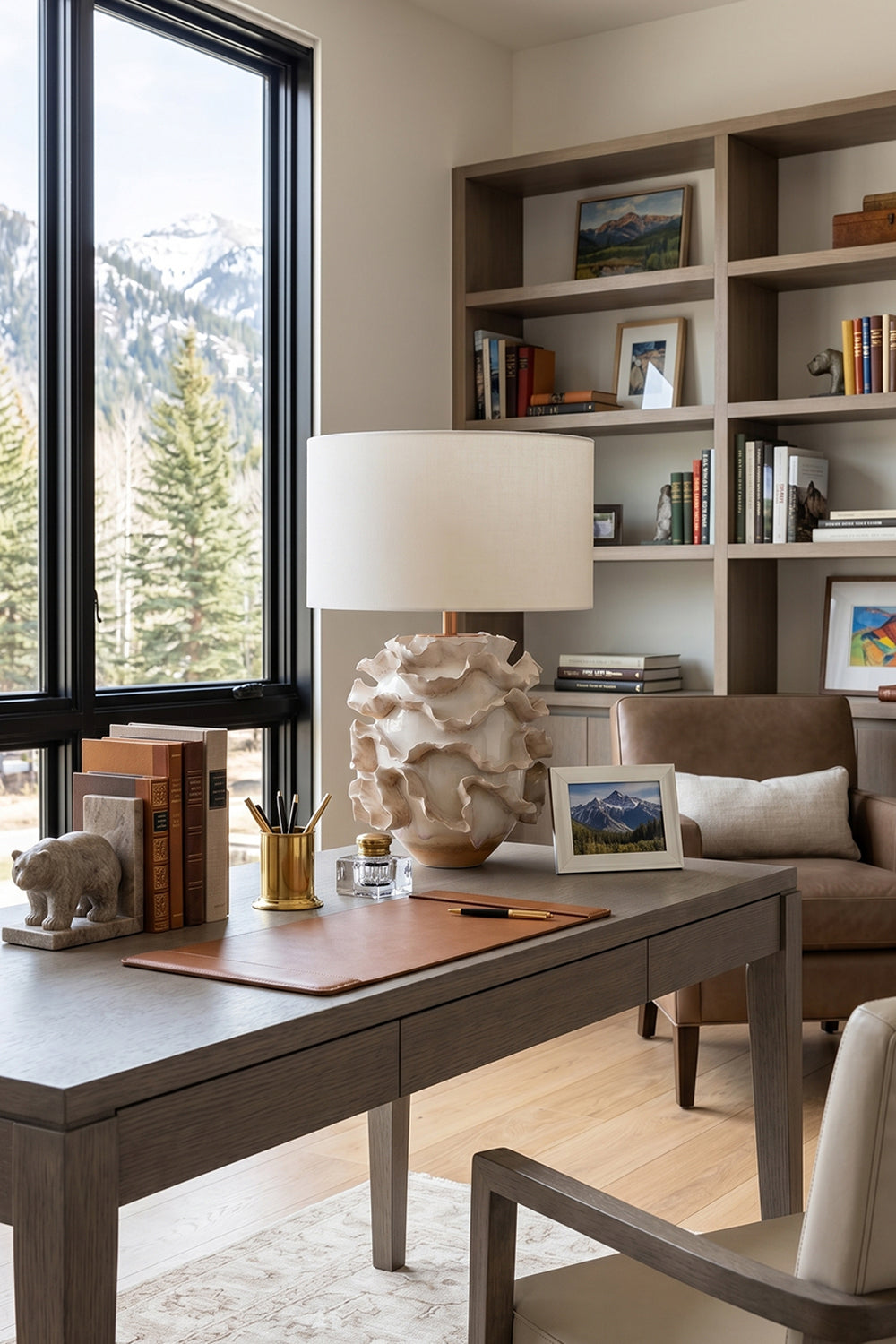 Coralia Ruffled Ceramic Table Lamp on a desk with shelves and a scenic mountain view in the background.