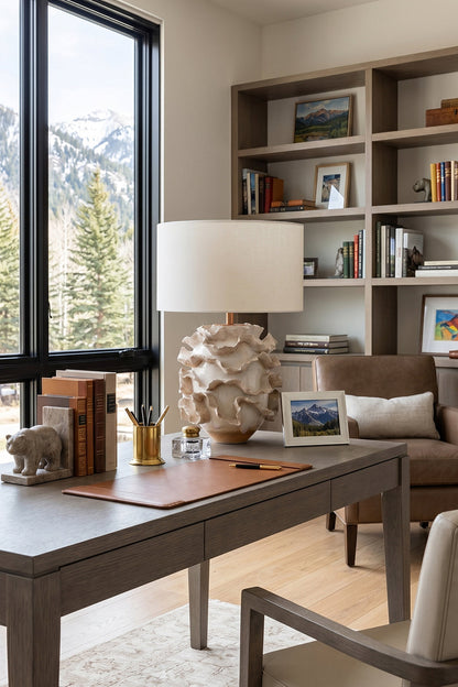 Coralia Ruffled Ceramic Table Lamp on a desk with shelves and a scenic mountain view in the background.