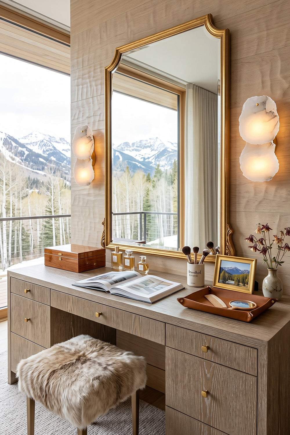 Corin Alabaster Wall Sconce illuminating a modern vanity with mountain view, featuring gold mirror and natural decor.