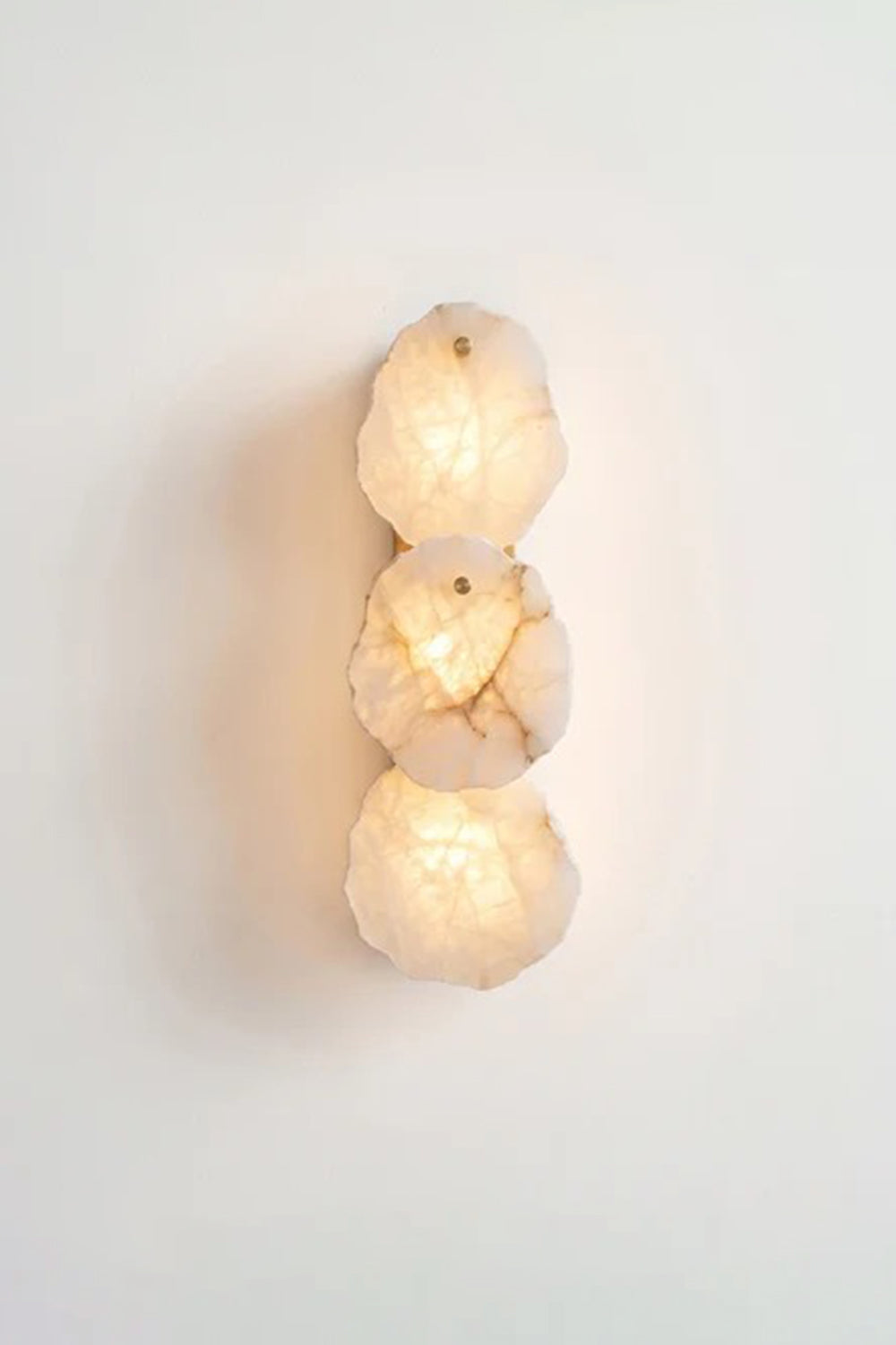 Corin Alabaster Wall Sconce featuring three illuminated alabaster shades on a white wall