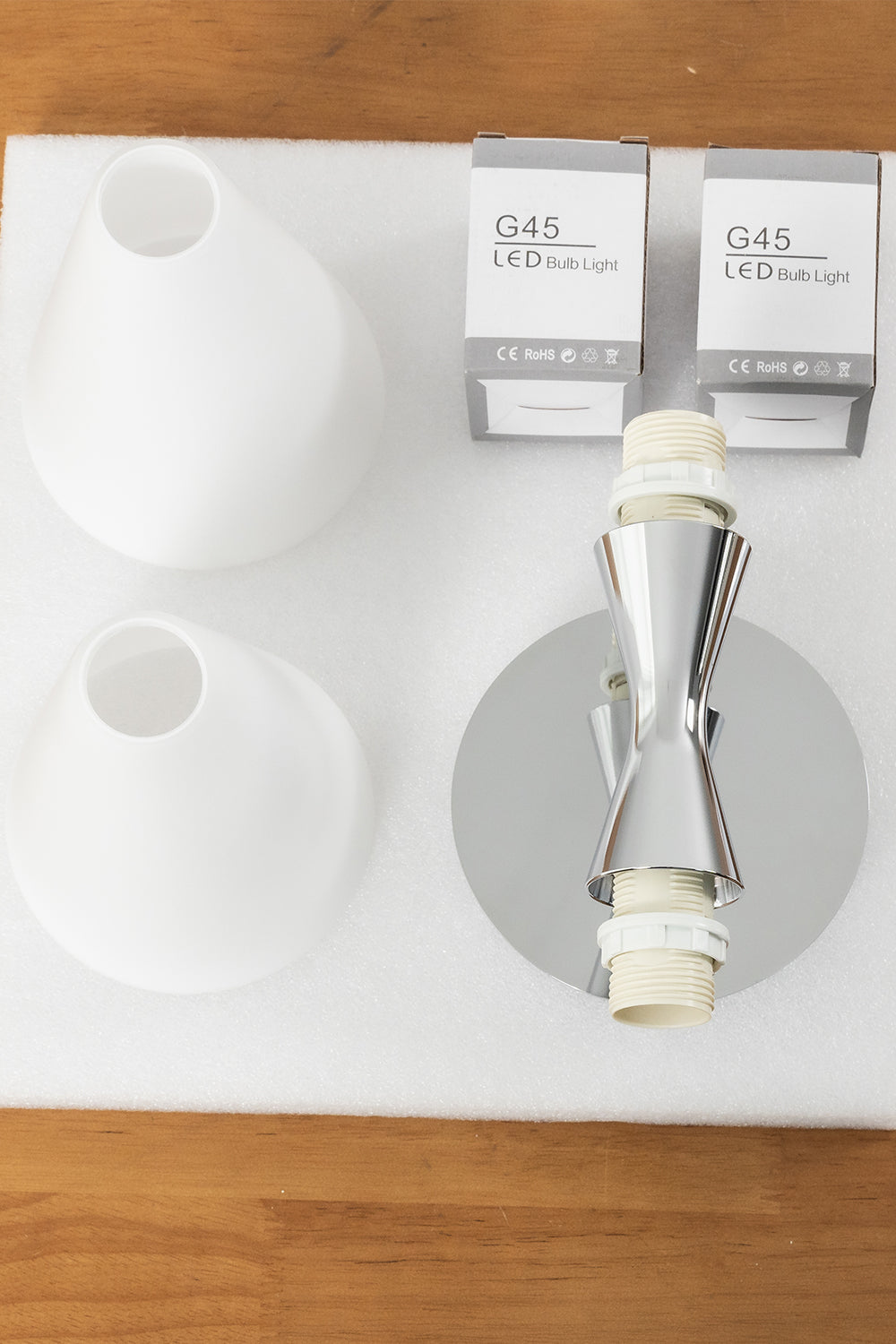 Diabolo Symmetry Glass Wall Sconce components including glass shades and LED bulbs on a wooden surface.