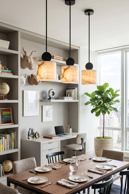 Elian Minimalist Alabaster Pendant Light hanging above a modern dining table with plants and bookshelves in the background.