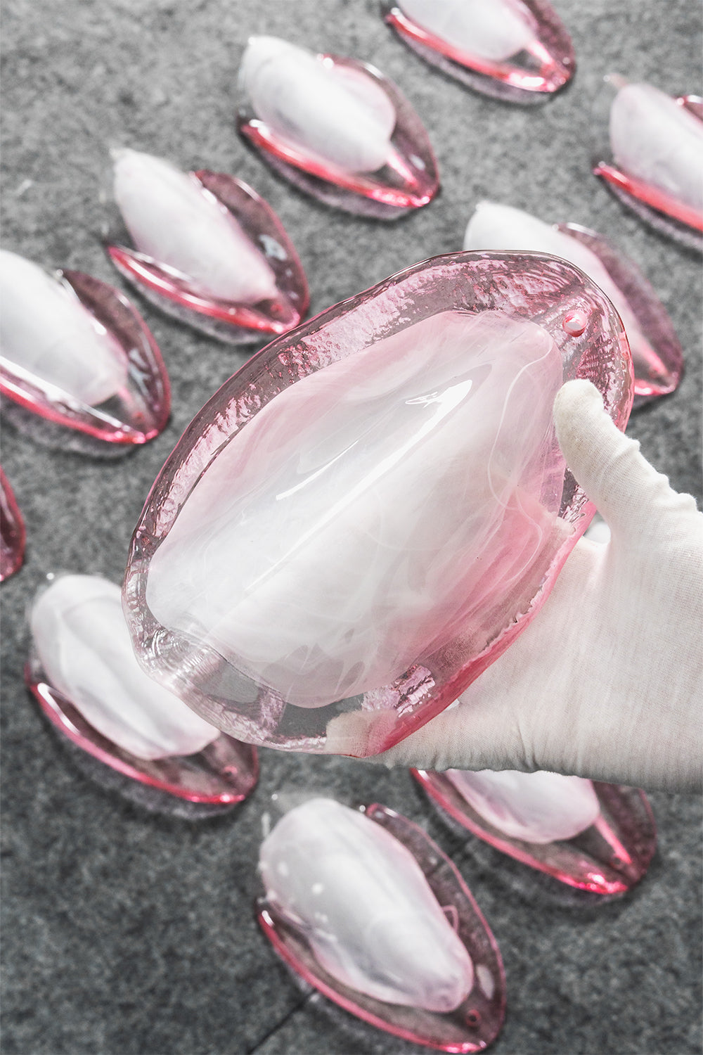 Elysian Bloom Rose Glass Chandelier | Metal, Glass | A gloved hand inspecting a single translucent pink glass petal surrounded by more glass components | Detail shot | vexa lamps