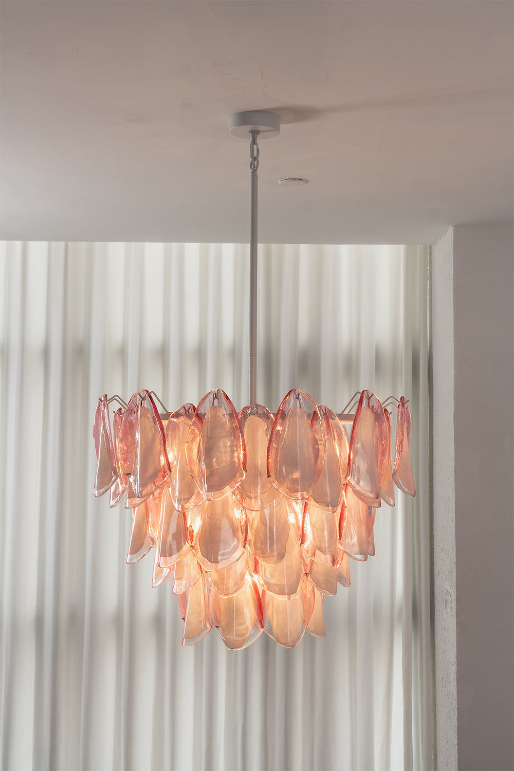 Elysian Bloom Rose Glass Chandelier | Metal, Glass | Fully lit chandelier casting a warm rosy glow in front of sheer white curtains | vexa lamps