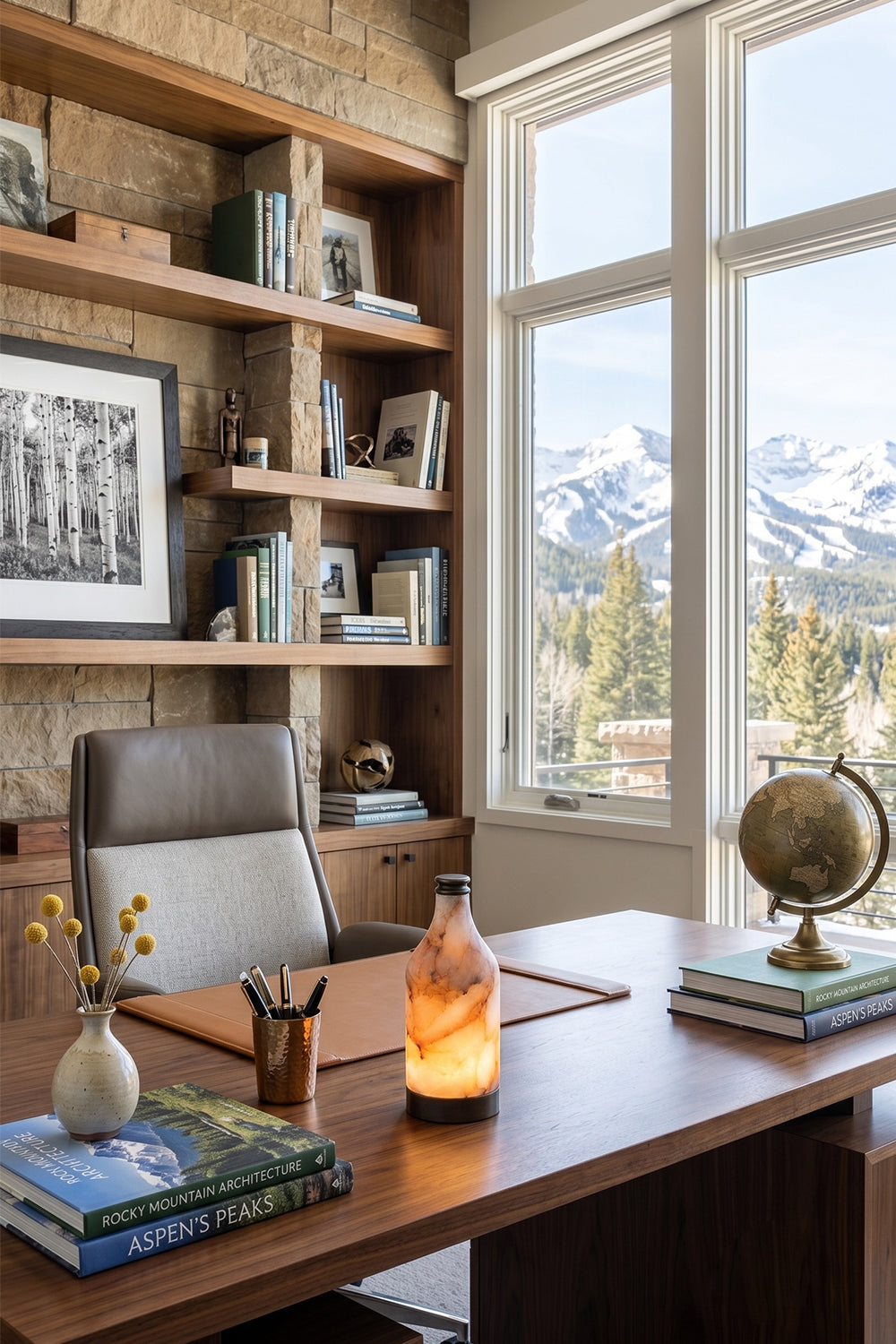 Evander Alabaster Bottle Table Lamp | Alabaster, Metal | Placed as cozy task lighting on a dark executive wooden desk in a rustic home library office with a scenic mountain view window | vexa lamps
