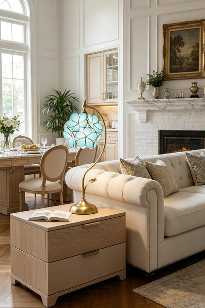 Evanthe Blossom Stained Glass Table Lamp | Stained Glass, Metal | Blue variant illuminating a cozy modern living room setup from a light beige side table next to a plush cream sofa | vexa lamps