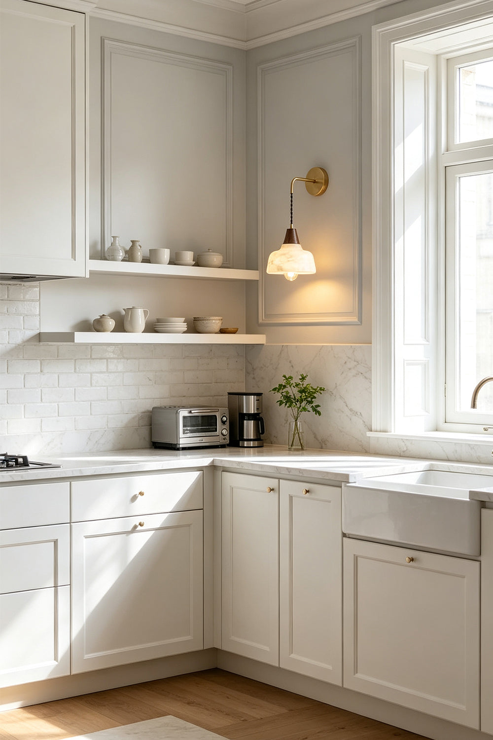 Everett Alabaster Hook-Arm Wall Sconce illuminating a stylish kitchen with white cabinets and shelves.