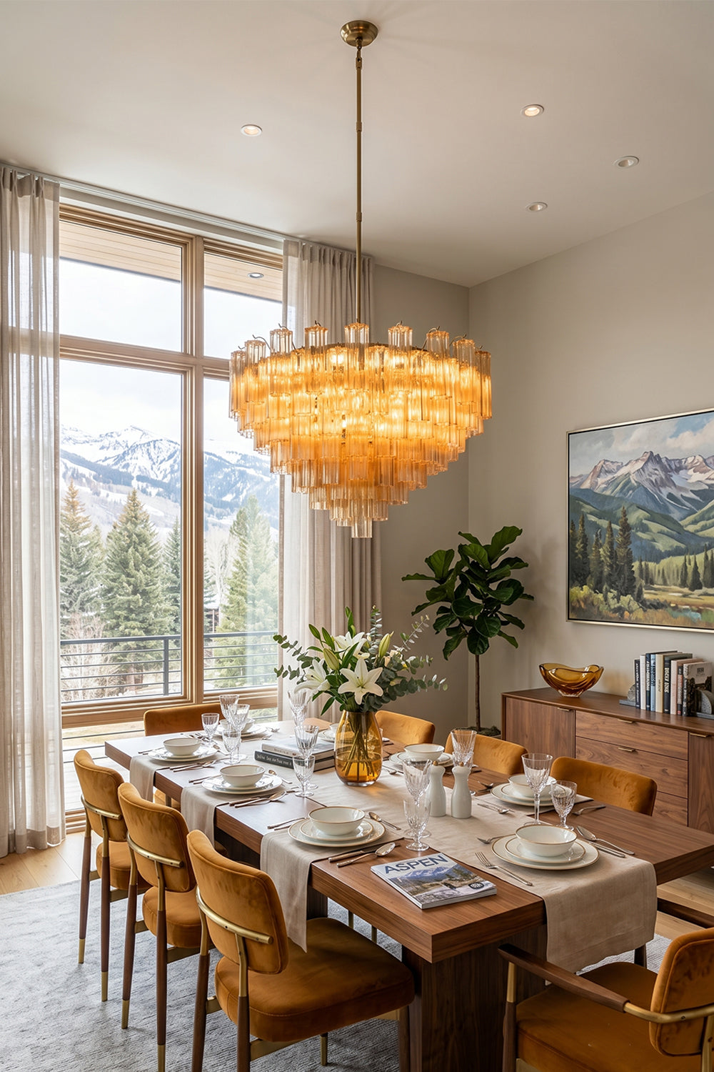 Isadora Tiered Amber Glass Chandelier illuminating a dining room with mountain views, showcasing mid-century glamour and elegance.