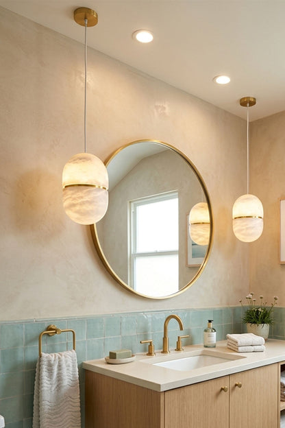 Isaline Banded Capsule Alabaster Pendant Light in modern bathroom with round mirror and gold fixtures.