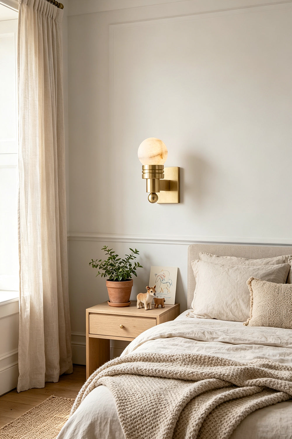 Isolde Alabaster Orb Wall Sconce | Natural Alabaster and Aged Brass | Installed as a bedtime reading light beside a cozy neatly made bed in a bedroom | vexa lamps