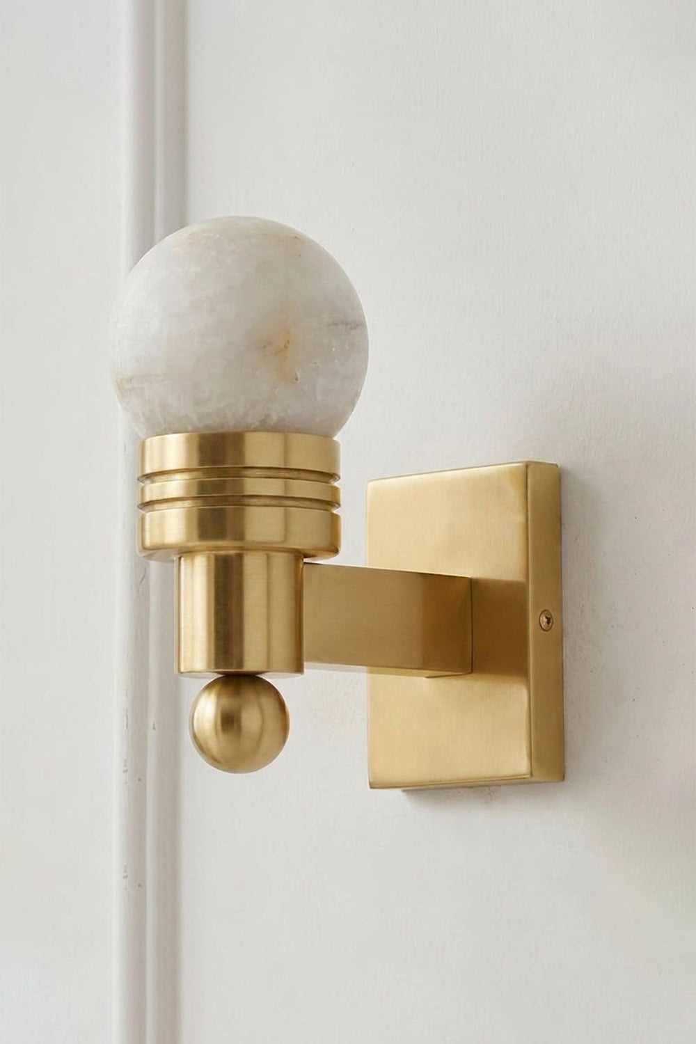 Isolde Alabaster Orb Wall Sconce | Natural Alabaster and Aged Brass | Full view of the elegant single wall lamp mounted on a clean light beige wall | vexa lamps