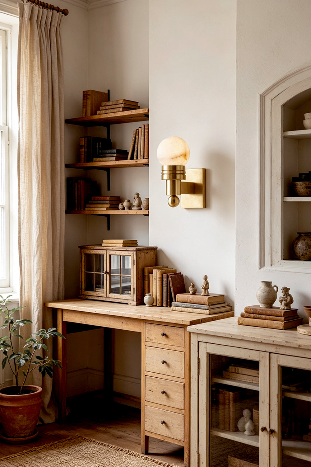 Isolde Alabaster Orb Wall Sconce | Natural Alabaster and Aged Brass | Mounted on a wall above a vintage wooden study desk and shelves in a warm room | vexa lamps