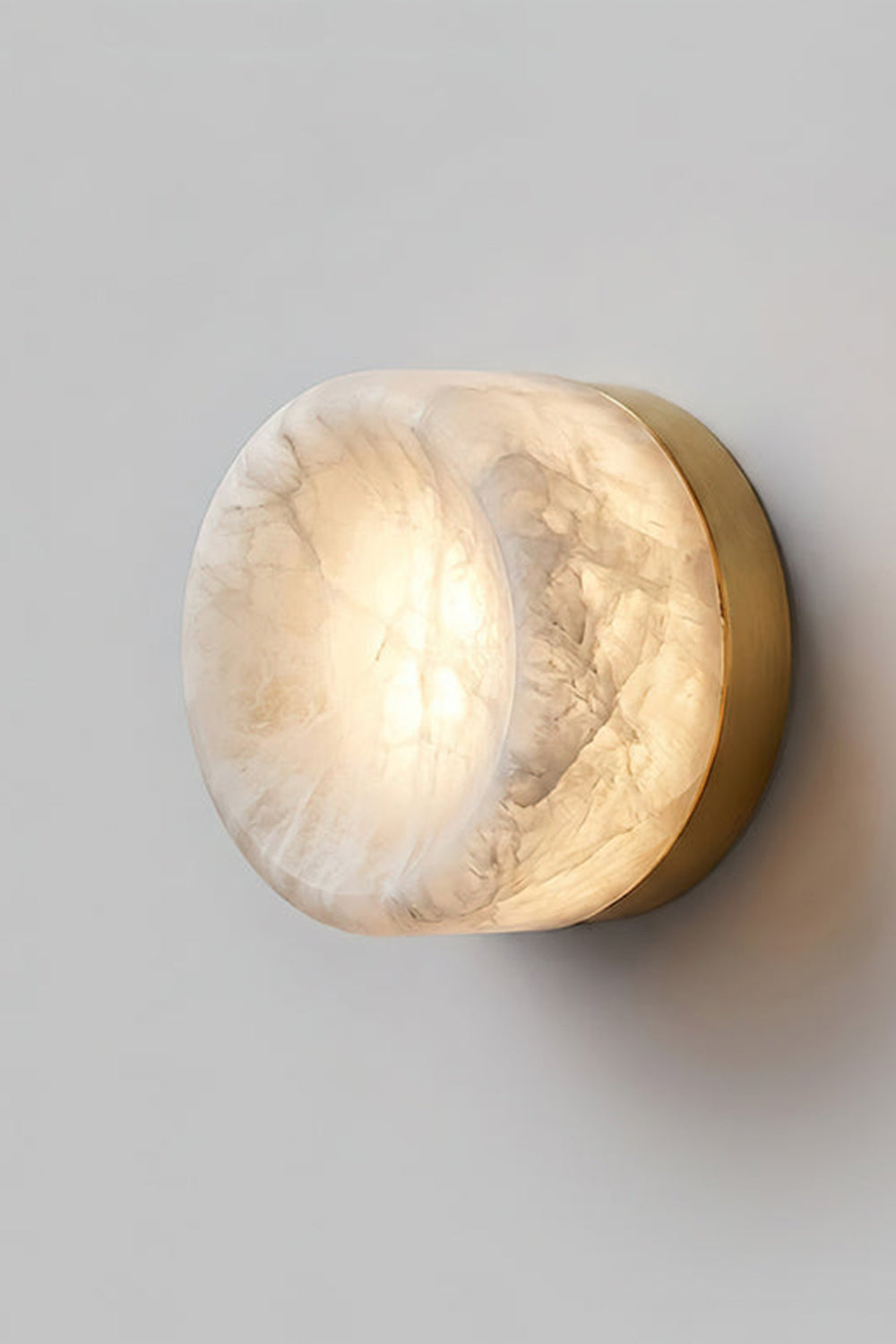 Isolde Concave Alabaster Disc Wall Sconce | Natural Alabaster and Black Metal | Studio close-up shot of the lit sconce featuring a matte black finish base on a light wall | vexa lamps