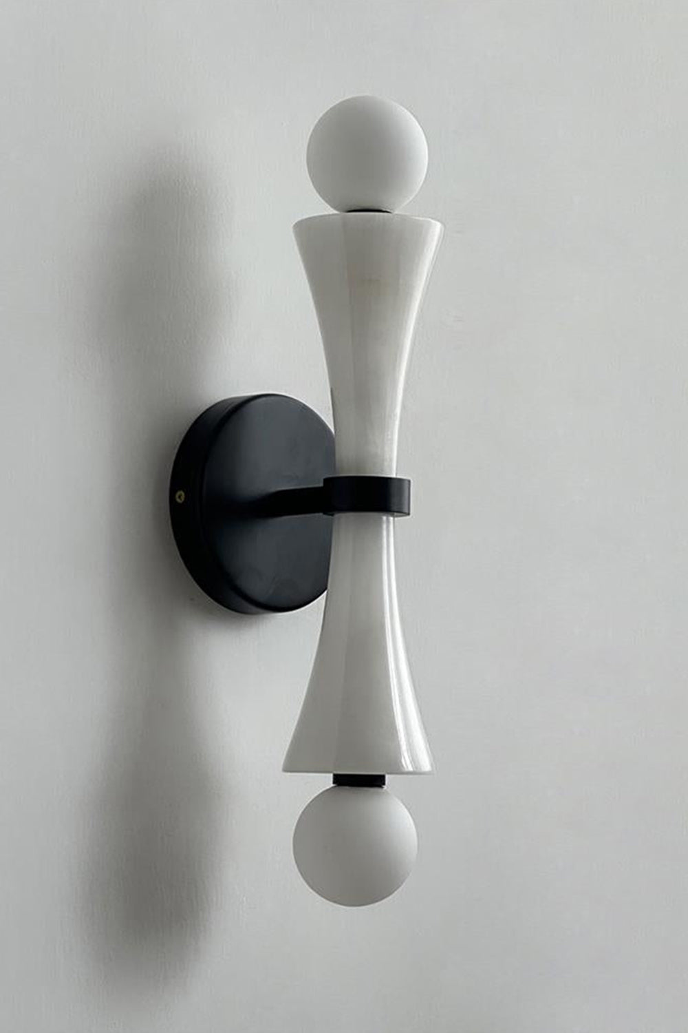 Katia Travertine Hourglass Wall Lamp | Travertine, Metal | Studio variant product view featuring a smooth white marble or stone hourglass body paired with black hardware fittings | vexa lamps