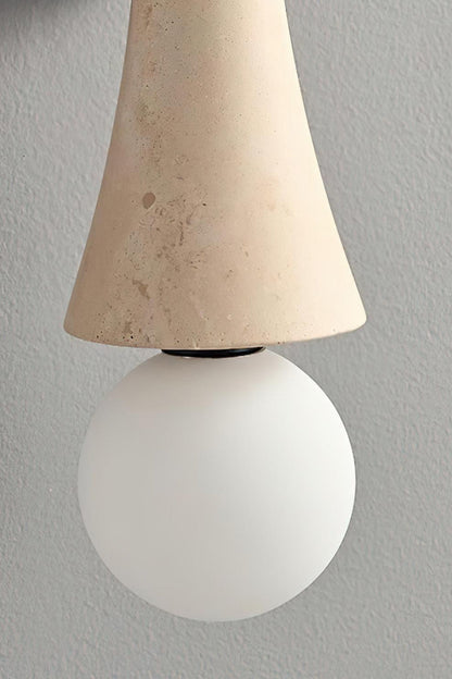 Katia Travertine Hourglass Wall Lamp | Travertine, Metal | Close-up focus on the white frosted glass globe bulb seamlessly meeting the tapered edge of the natural porous travertine stone shade | Detail shot | vexa lamps
