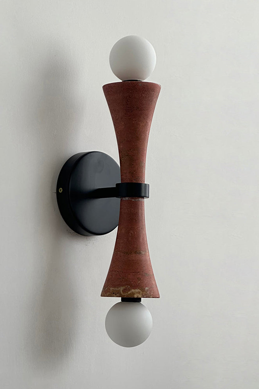 Katia Travertine Hourglass Wall Lamp | Travertine, Metal | Studio variant product view featuring a rich reddish-brown terracotta colored stone hourglass body paired with black hardware | vexa lamps