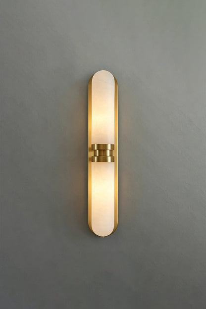 Linea Alabaster Capsule Wall Sconce | Alabaster, Brass | Frontal studio view of the fully lit linear capsule stone sconce casting a warm glow against a minimalist grey background | vexa lamps