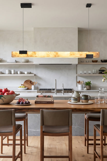Liora Linear Alabaster Pendant Light | Natural Alabaster and Black Metal | Casting a warm ambient glow over a wooden kitchen counter and elegant high-back bar chairs | vexa lamps