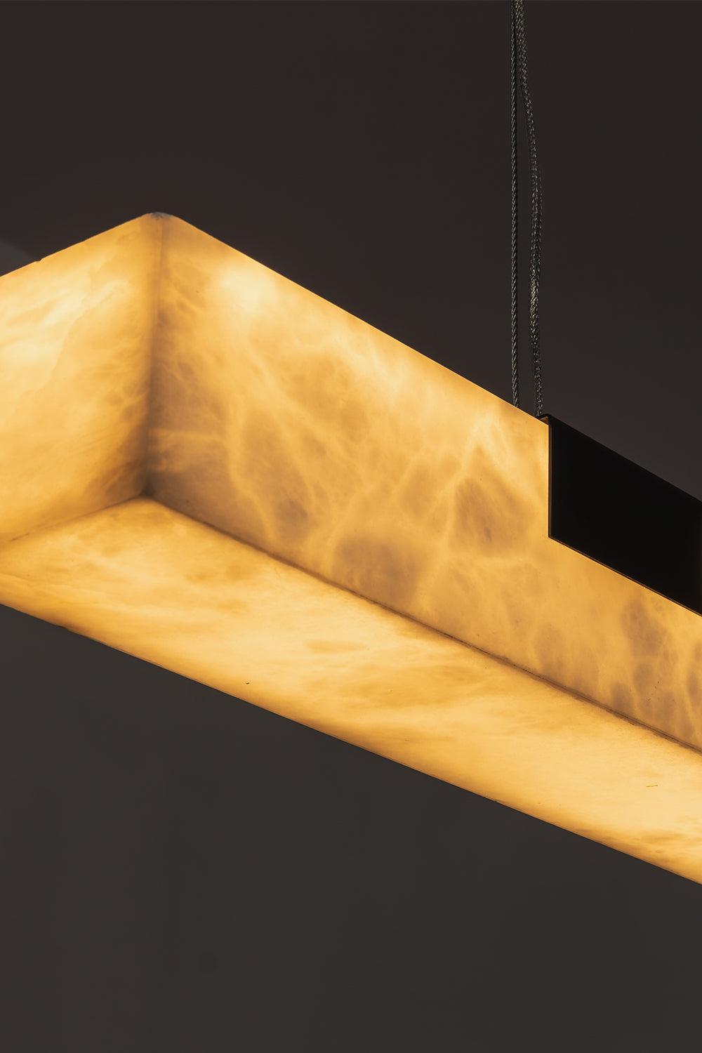 Liora Linear Alabaster Pendant Light | Natural Alabaster and Black Metal | Close-up macro view highlighting the corner of the glowing alabaster stone and a black bracket | vexa lamps
