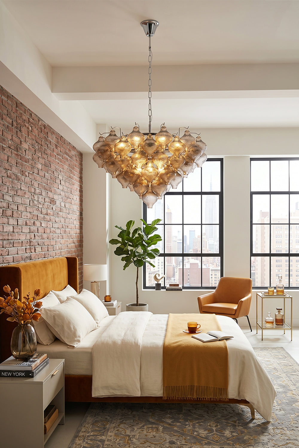 Lucina Tiered Smoked Glass Chandelier illuminating a stylish bedroom with brick walls and elegant furnishings.