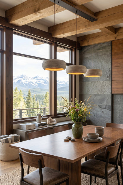 Maro Travertine Donut Pendant Light | Travertine, Metal | Three stone pendant lamps hanging over a long wooden dining table setup in a luxury mountain lodge dining room with large windows | vexa lamps