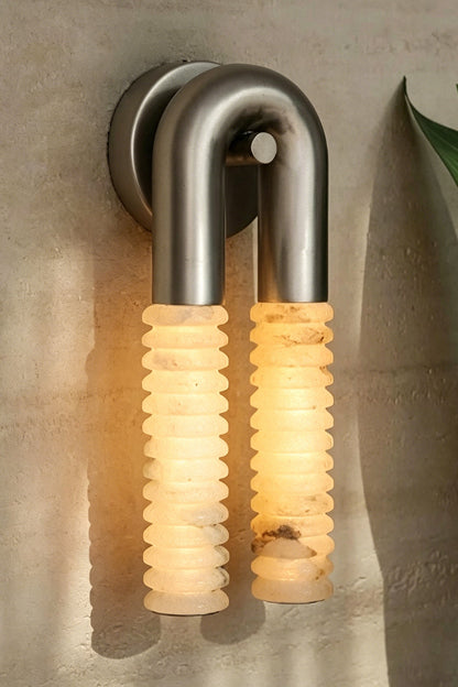 Monolith Arc Alabaster Wall Lamp | Alabaster, Metal | Side profile showing the depth of the metal arc and ribbed stone tubes on a textured wall | vexa lamps