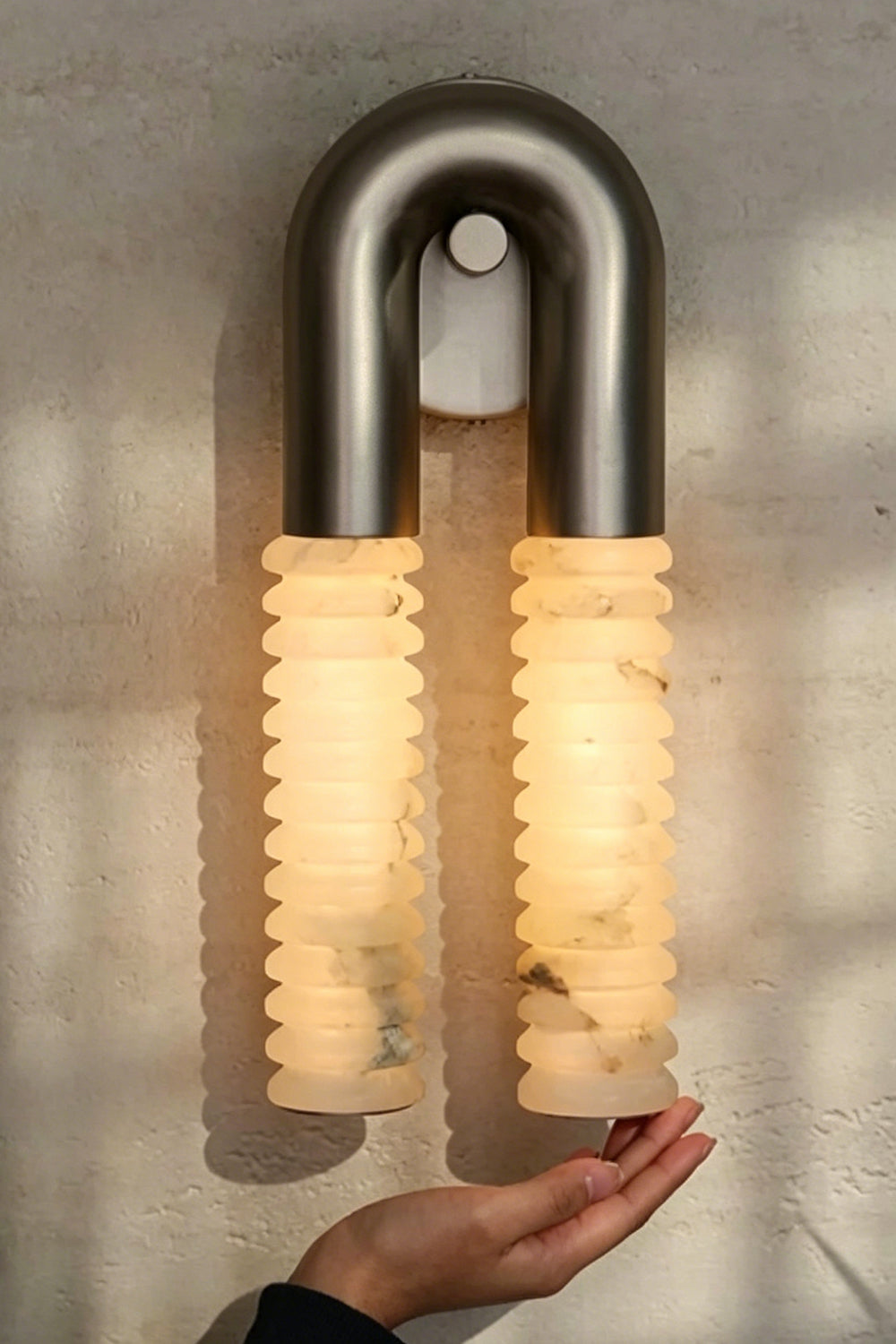 Monolith Arc Alabaster Wall Lamp | Alabaster, Metal | Fully lit lamp showing the warm translucency and scale next to a person's hand | Detail shot | vexa lamps